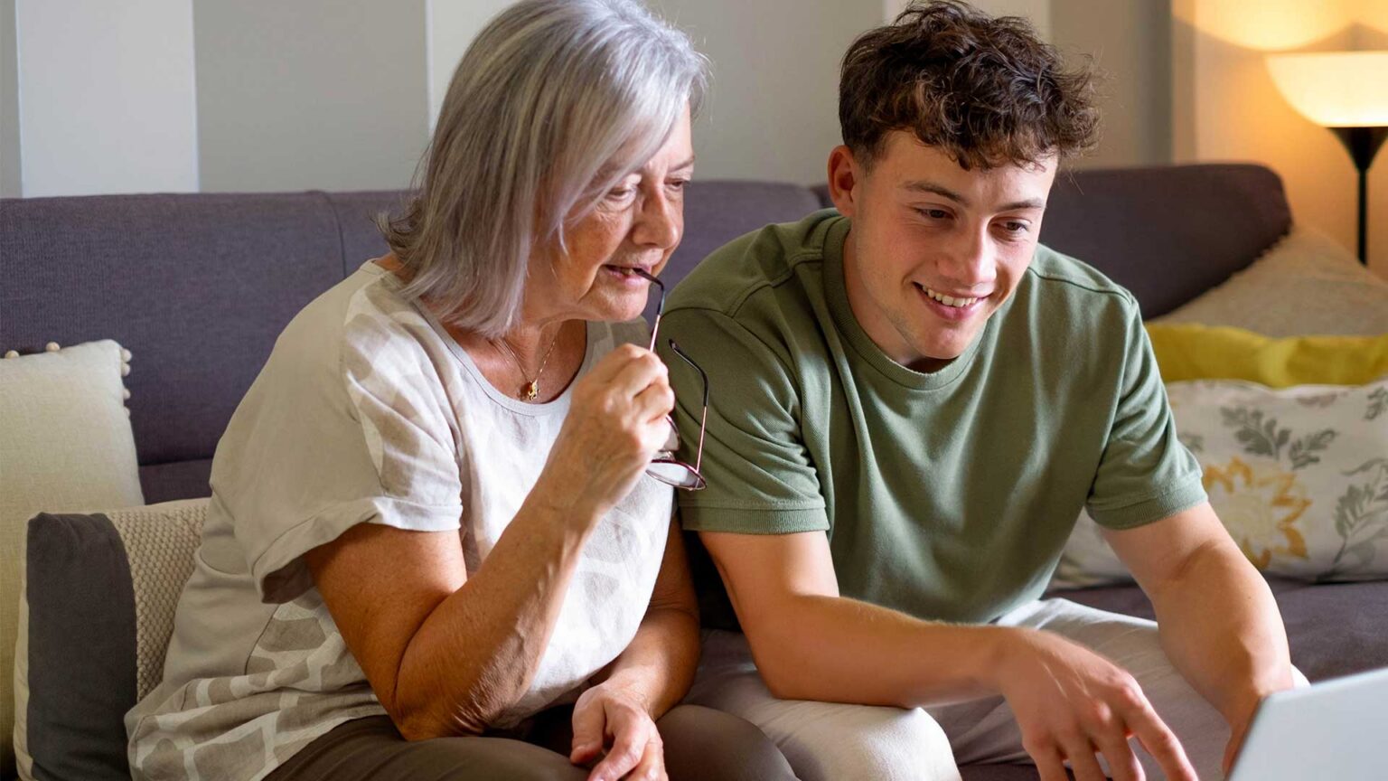 Elderly woman and a young man sitting on a couch and looking at a screen.
